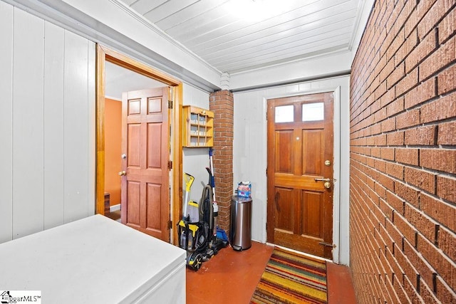 entrance foyer with wood walls, ornamental molding, and brick wall