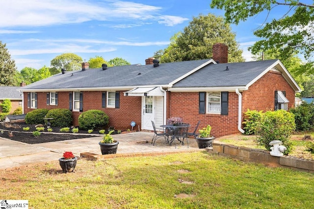 rear view of property featuring a patio, a chimney, roof with shingles, a lawn, and brick siding