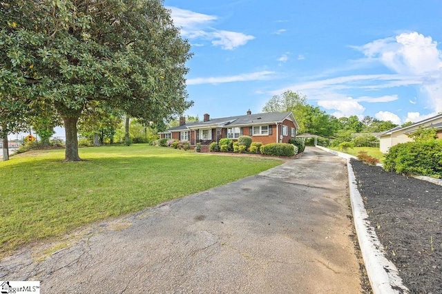 ranch-style house featuring a chimney, concrete driveway, brick siding, and a front lawn