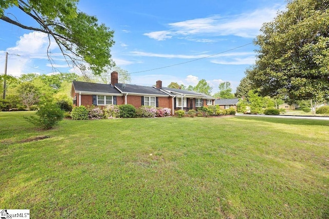 ranch-style home with a chimney, brick siding, and a front lawn