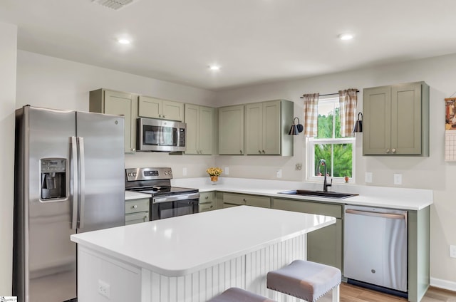 kitchen with a sink, gray cabinetry, light countertops, stainless steel appliances, and a kitchen island