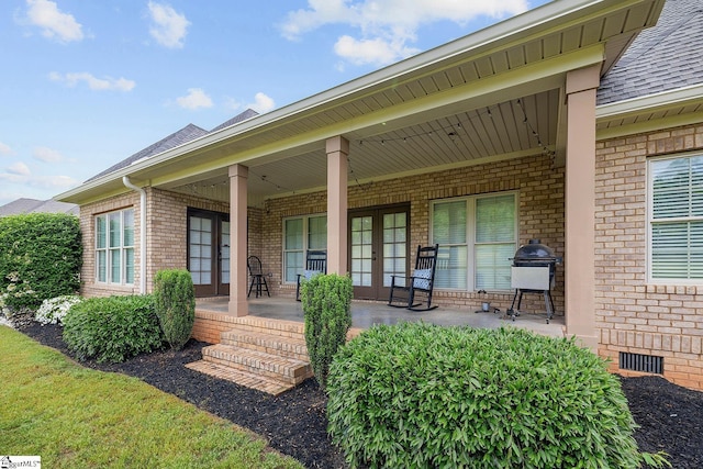 view of exterior entry with brick siding, visible vents, crawl space, french doors, and roof with shingles