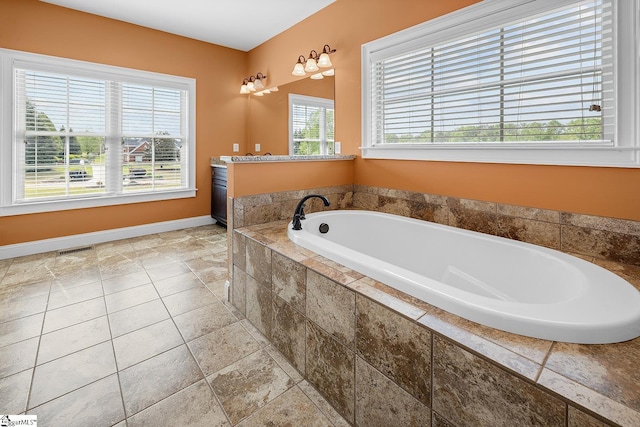 bathroom featuring stone tile floors, visible vents, plenty of natural light, and a bath
