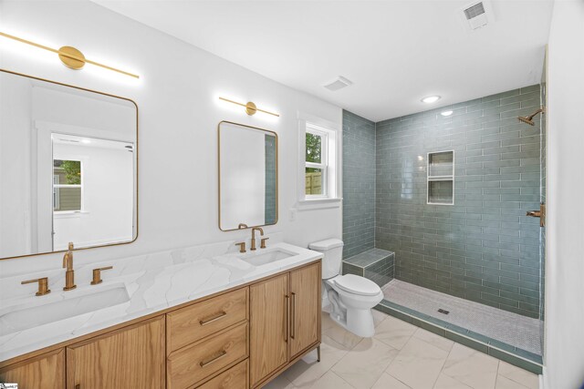 bathroom featuring a tile shower, toilet, double vanity, and a sink