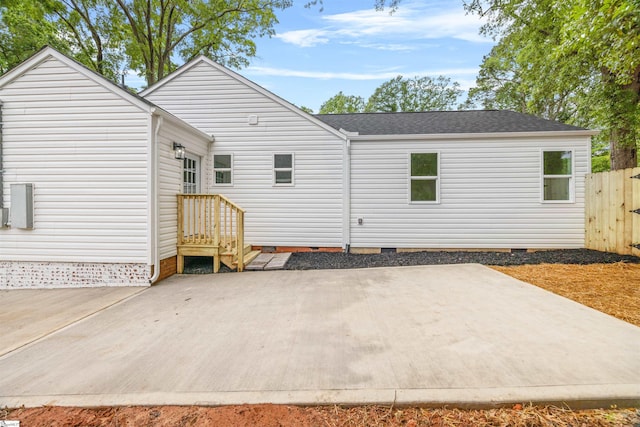 back of property with fence, a patio area, a shingled roof, and crawl space
