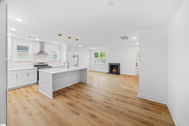 kitchen with recessed lighting, light wood-type flooring, wall chimney exhaust hood, visible vents, and gas range