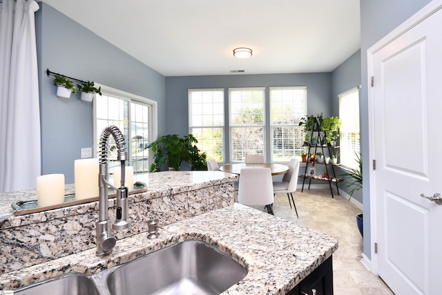 kitchen featuring baseboards, visible vents, light stone counters, and a sink