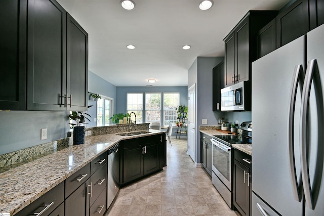 kitchen with light stone counters, a sink, stainless steel appliances, a peninsula, and dark cabinetry