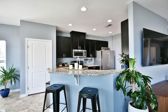kitchen featuring light stone counters, a breakfast bar, visible vents, stainless steel appliances, and dark cabinetry