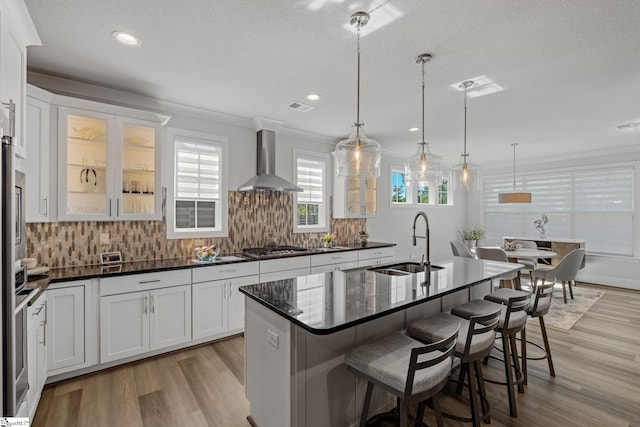 kitchen with light wood-type flooring, wall chimney exhaust hood, backsplash, and a sink