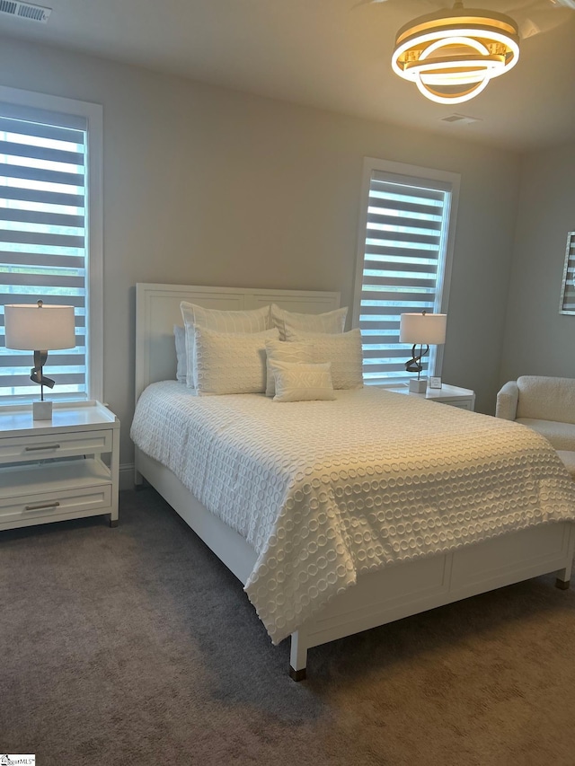bedroom with visible vents, dark colored carpet, and multiple windows