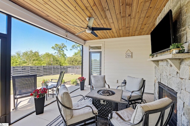 sunroom featuring a ceiling fan, an outdoor stone fireplace, and a fire pit