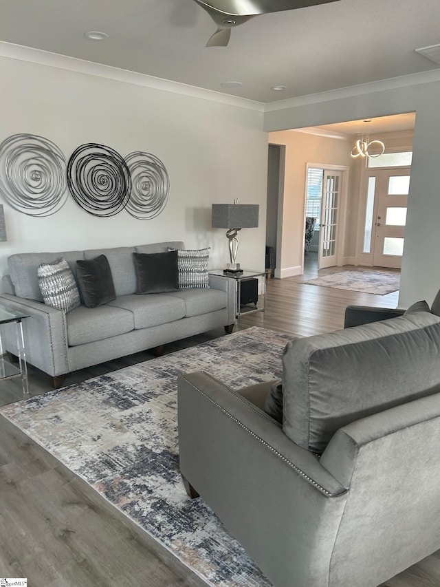 living room featuring wood finished floors, crown molding, ceiling fan with notable chandelier, and baseboards
