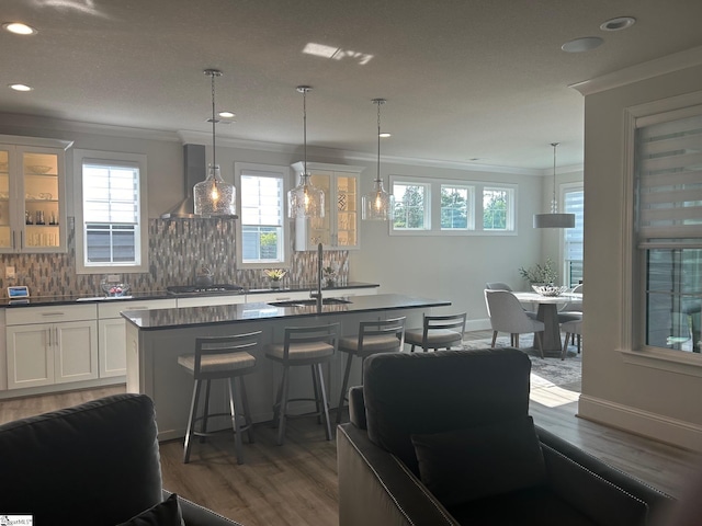 kitchen featuring a sink, a kitchen bar, tasteful backsplash, wall chimney exhaust hood, and dark countertops