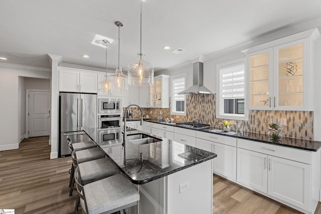 kitchen with a sink, appliances with stainless steel finishes, light wood finished floors, ornamental molding, and wall chimney exhaust hood