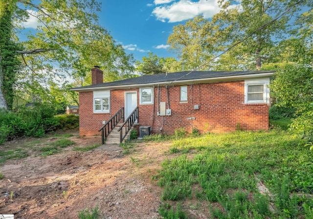 rear view of house featuring brick siding, central AC unit, entry steps, and a chimney