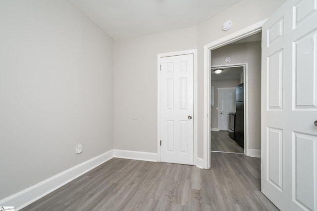 unfurnished bedroom with wood finished floors, freestanding refrigerator, and baseboards