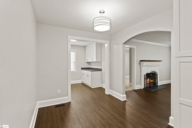 unfurnished living room with visible vents, baseboards, arched walkways, dark wood-style flooring, and a brick fireplace