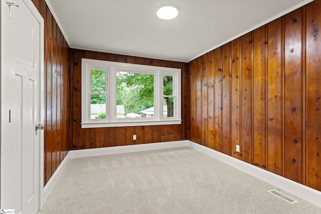 empty room featuring visible vents, wooden walls, crown molding, and carpet flooring