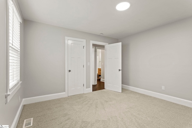 unfurnished bedroom with baseboards, visible vents, multiple windows, and carpet flooring