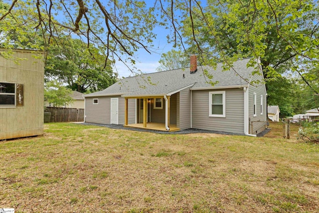 back of house with a chimney, fence, roof with shingles, and a lawn