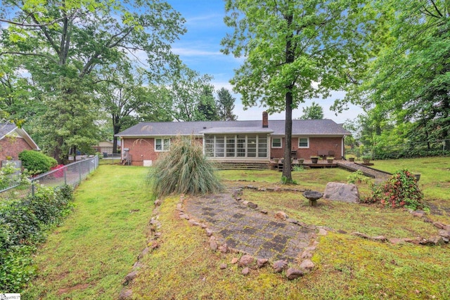 rear view of house with a chimney, brick siding, a fenced backyard, and a sunroom