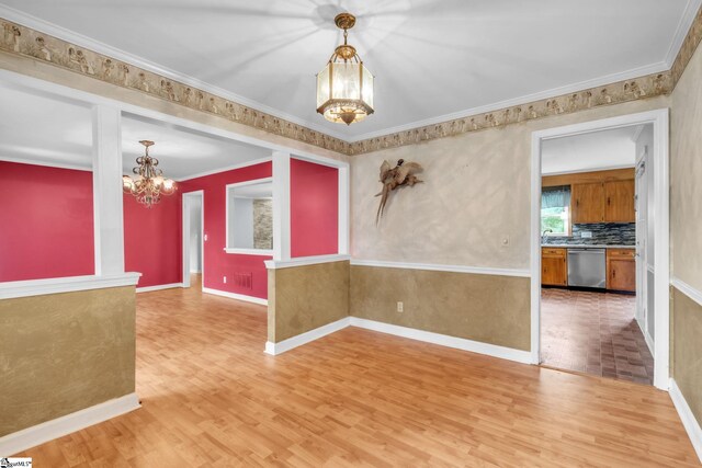 unfurnished room with an inviting chandelier, crown molding, light wood finished floors, and baseboards