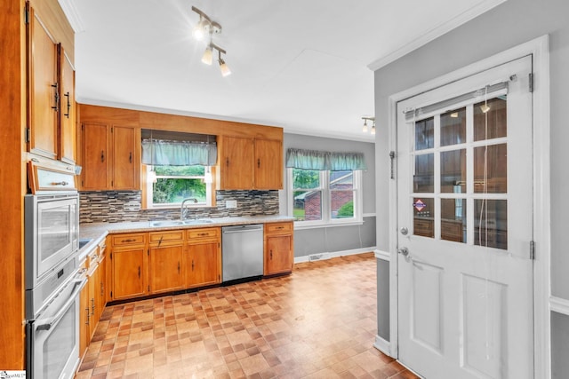 kitchen with a sink, decorative backsplash, brown cabinetry, light countertops, and appliances with stainless steel finishes
