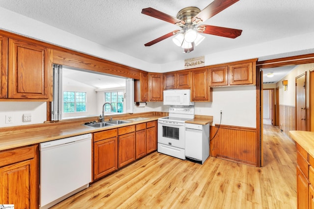 kitchen with brown cabinetry, white appliances, light wood-style floors, and a sink