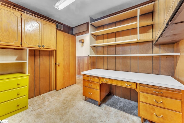 unfurnished office with built in desk, visible vents, and wood walls