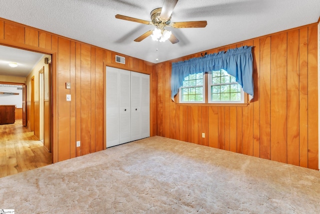 unfurnished bedroom featuring wooden walls, visible vents, carpet, and a closet