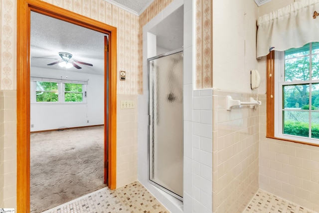 bathroom featuring a shower stall, ceiling fan, wallpapered walls, tile walls, and wainscoting