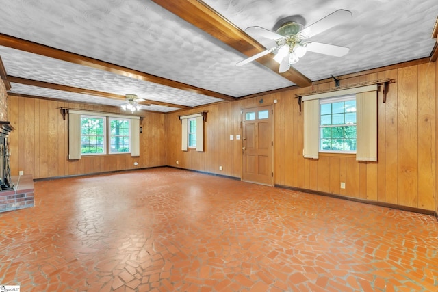 unfurnished living room featuring beam ceiling, wood walls, a ceiling fan, and plenty of natural light