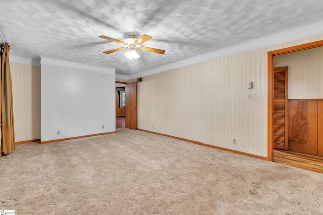 spare room with carpet, ceiling fan, crown molding, and baseboards