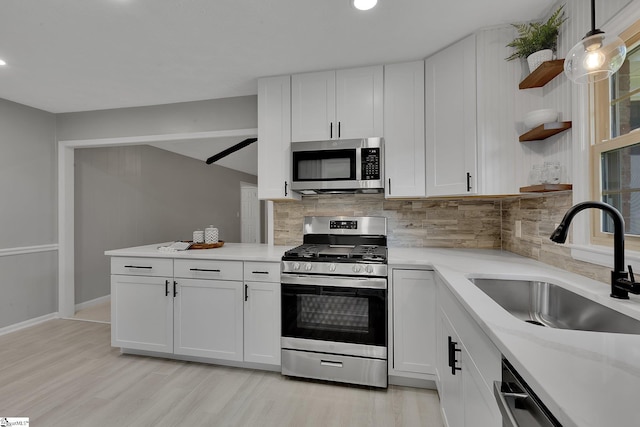 kitchen with open shelves, appliances with stainless steel finishes, light countertops, white cabinets, and a sink