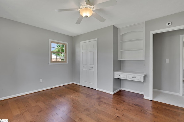 unfurnished bedroom with dark wood-style floors, baseboards, ceiling fan, and built in study area