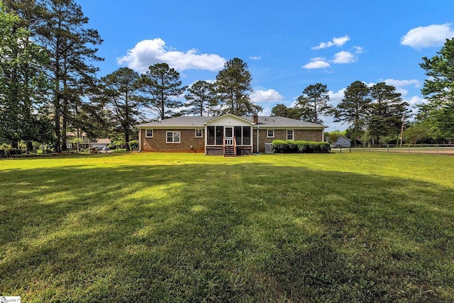 rear view of property featuring a lawn, fence, brick siding, and a sunroom