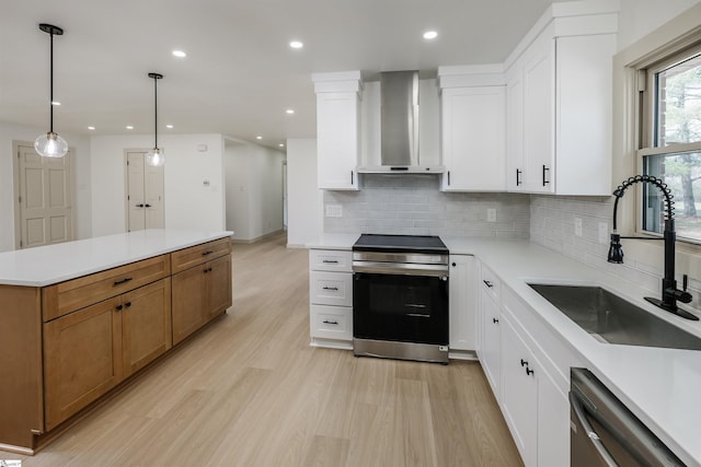 kitchen with tasteful backsplash, stainless steel appliances, wall chimney range hood, a sink, and light wood-type flooring