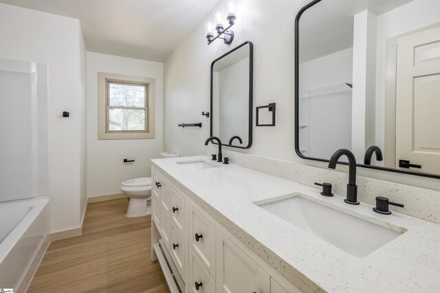bathroom featuring wood finished floors, toilet, baseboards, and a sink