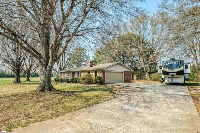 ranch-style home with concrete driveway, a chimney, an attached garage, brick siding, and a front lawn