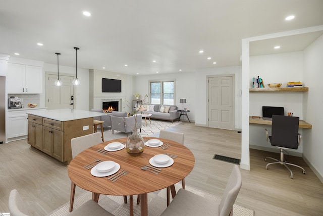 dining area featuring baseboards, light wood-type flooring, a warm lit fireplace, and recessed lighting