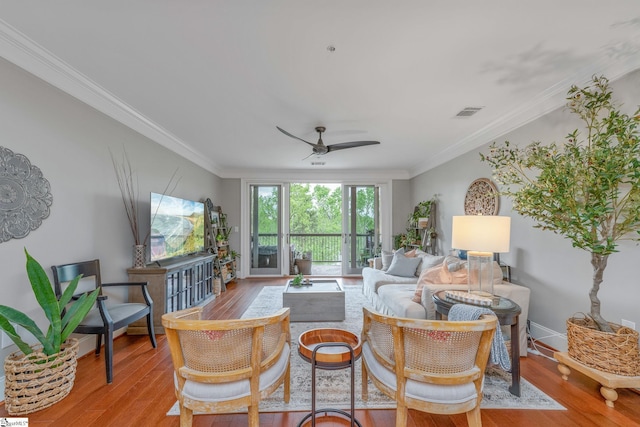 living room featuring crown molding, visible vents, baseboards, wood finished floors, and a ceiling fan