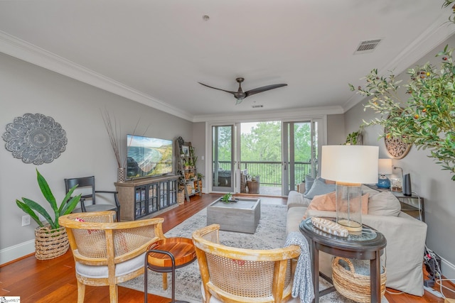 living area with wood finished floors, visible vents, a ceiling fan, and ornamental molding
