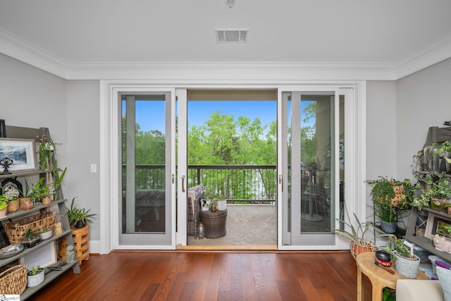 doorway with wood finished floors, visible vents, ornamental molding, and baseboards