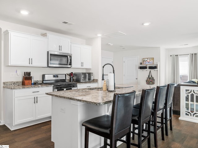 1087 Summerlin Trl, Duncan, SC 29334 - kitchen with a kitchen island with sink, light stone countertops, stainless steel appliances, dark wood-type flooring, and white cabinets