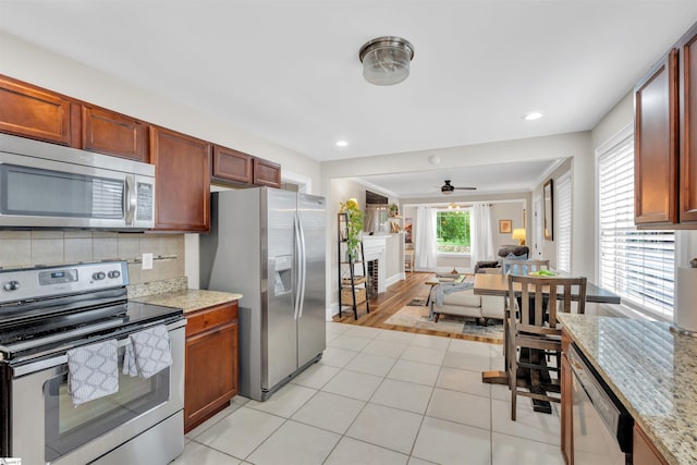 kitchen with light stone counters, decorative backsplash, ceiling fan, stainless steel appliances, and open floor plan