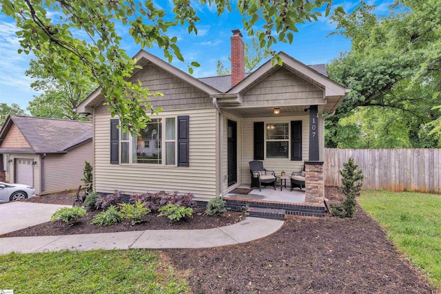 bungalow-style house featuring a porch, fence, and a chimney
