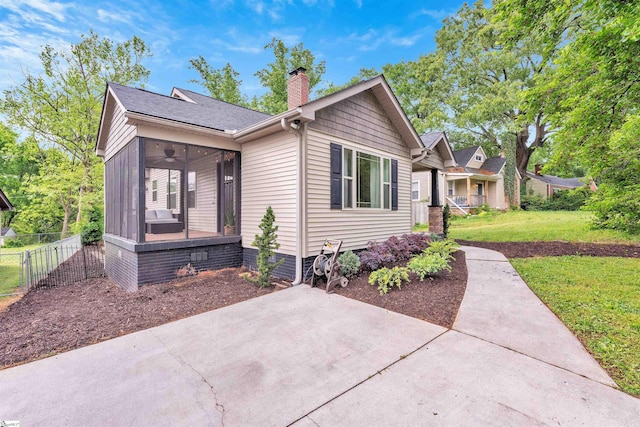 view of front of house with a chimney, fence, ceiling fan, a sunroom, and a front yard