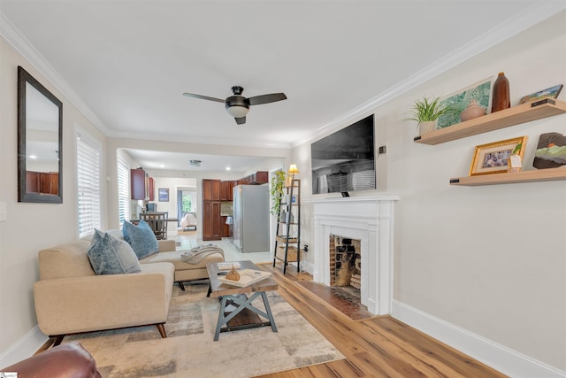 living room with a fireplace, light wood-style floors, ceiling fan, crown molding, and baseboards