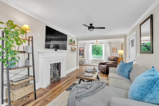 living room featuring a fireplace with flush hearth, crown molding, a ceiling fan, baseboards, and wood finished floors